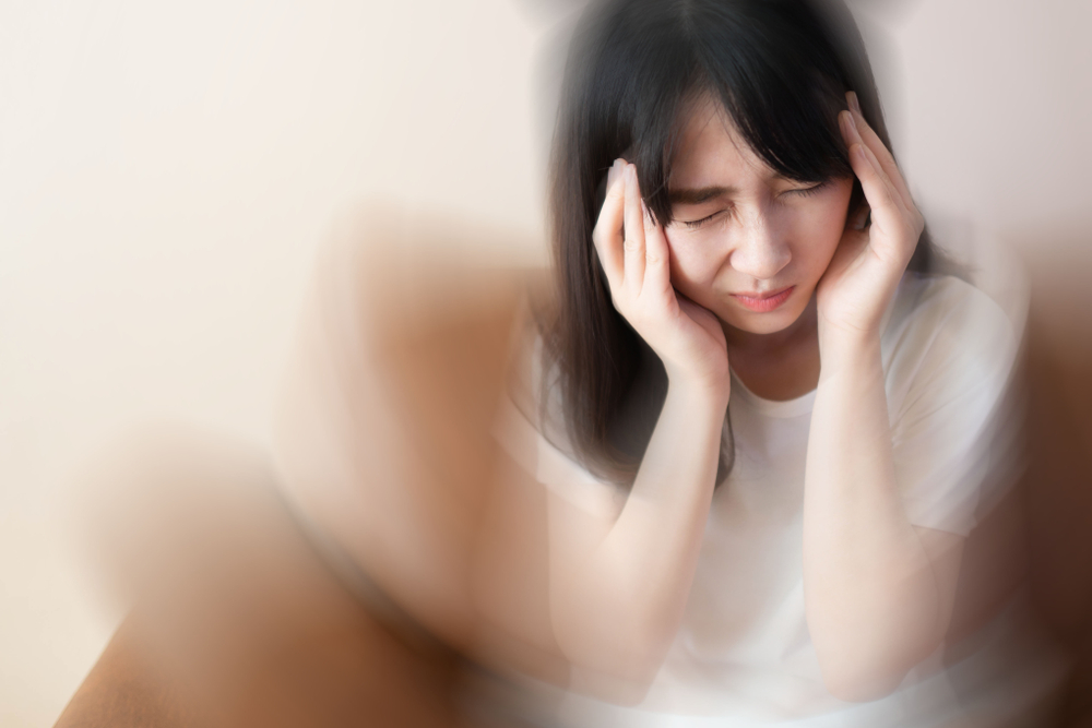 Young female suffering from dizziness, vertigo, headache while sitting on couch at home. Cause of dizzy inclued migraine, stress, stroke, BPPV, Meniereâs disease or brain tumor. Health care problem.