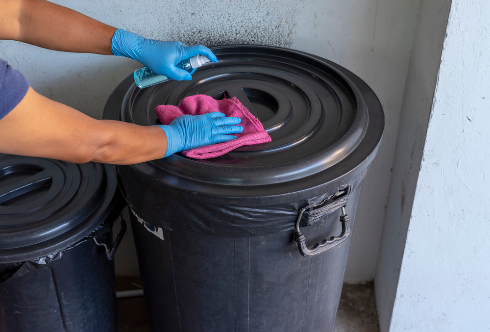 Female Staff disinfecting garbage bin by spraying a blue sanitizer from the bottle on wet wipe. Antiseptic,disinfection,cleanliness and healthcare. Anti bacterial amd Corona virus (COVID-19). 
