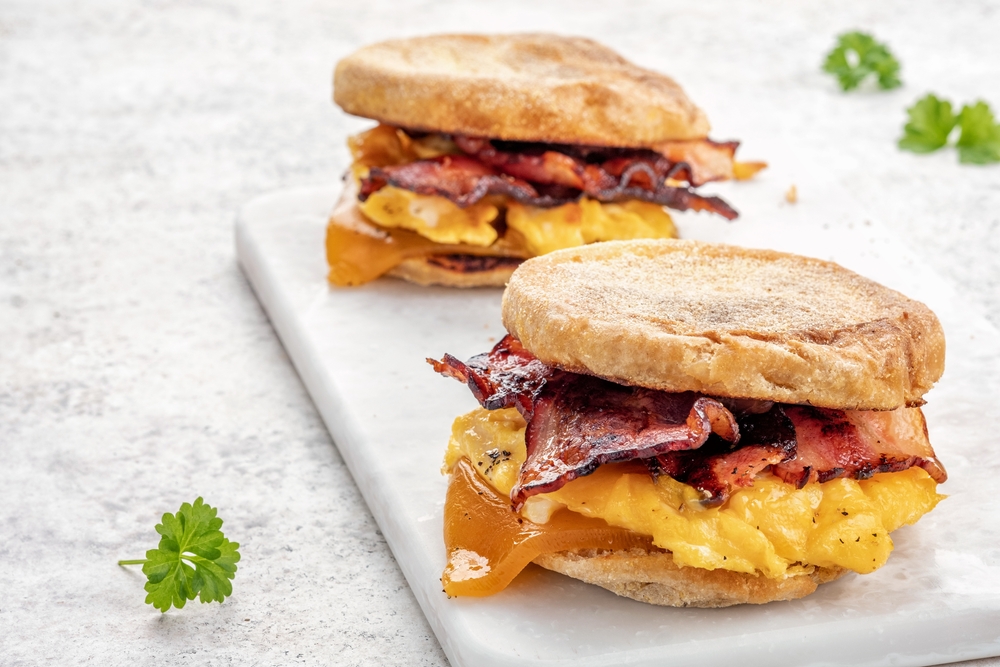 English muffin, scrumbled egg, ham, and cheese breakfast sandwich on a cutting board