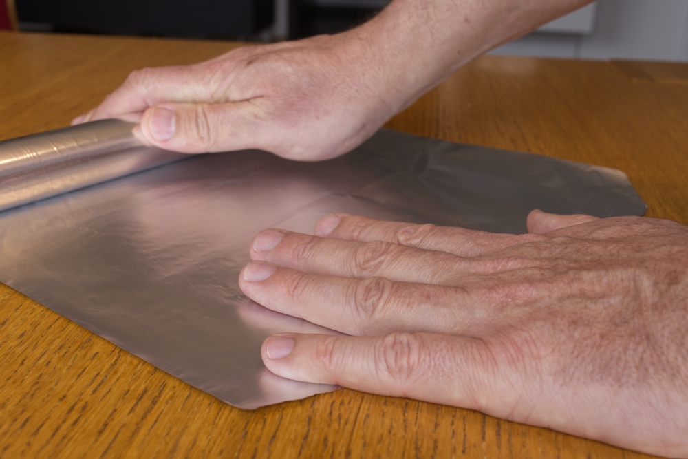 Men hands roll off the aluminum foil for household use on a wooden surface.  