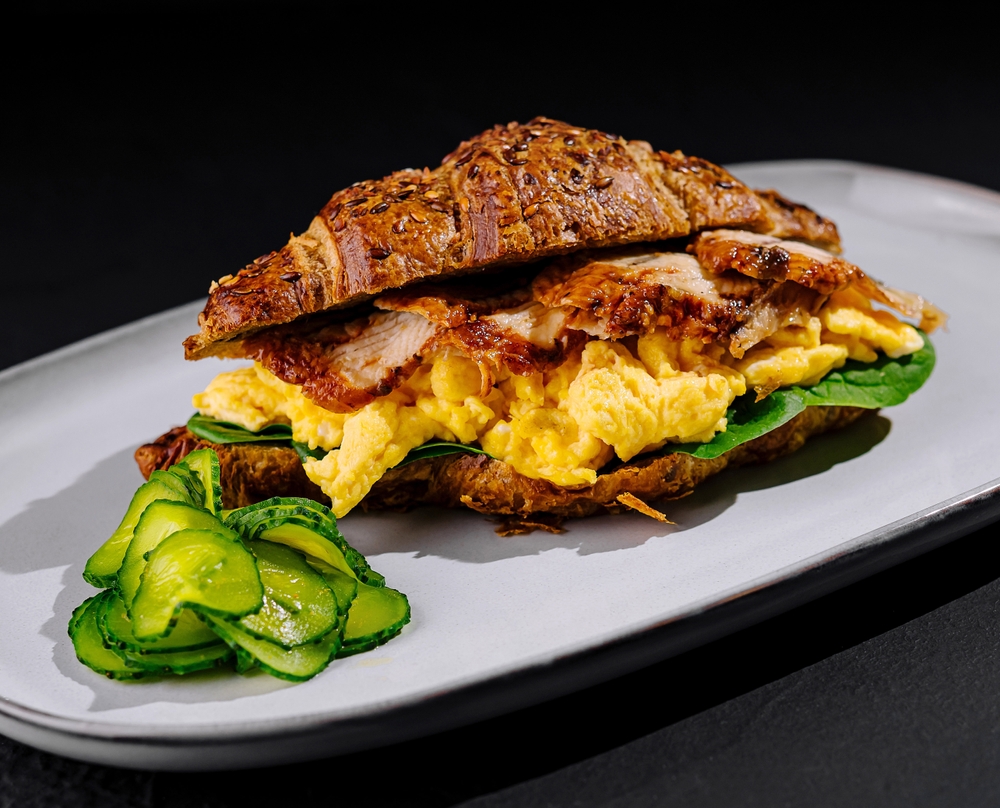Delicious gourmet croissant breakfast sandwich with scrambled eggs. Bacon. And avocado on a freshly baked croissant. Perfect for a savory and healthy morning meal. Ideal for brunch