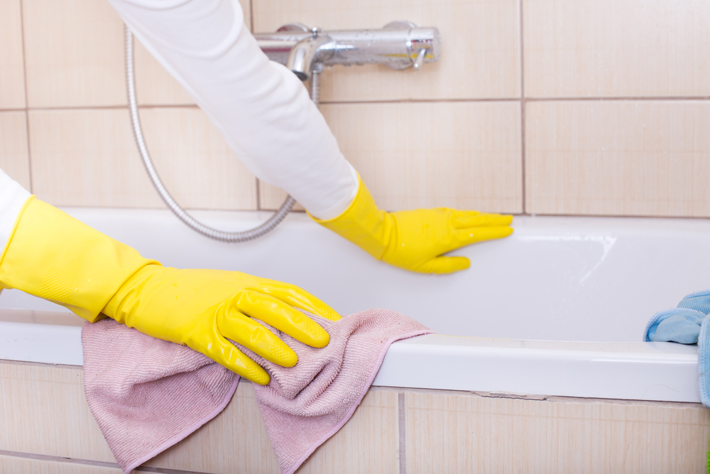 Close up of female hands with rubber gloves cleaning bathtub