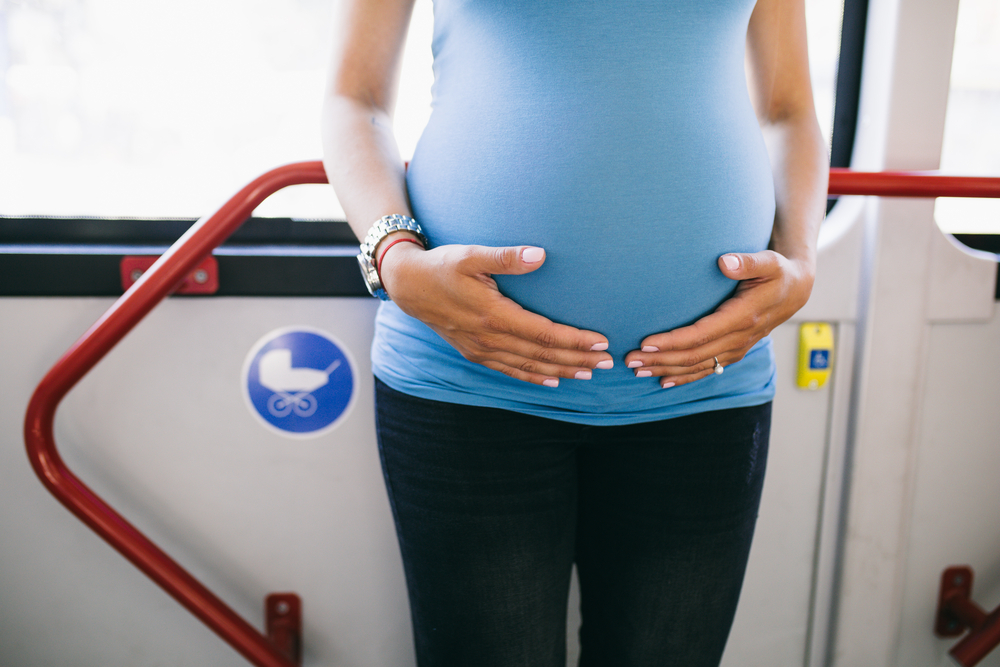Beautiful young pregnant woman standing in city bus.