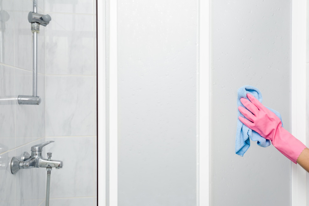 Employee's hand in rubber protective glove with rag washing and polishing a shower doors. Maid or housewife cares about house. Spring general or regular clean up. Commercial cleaning company concept. 