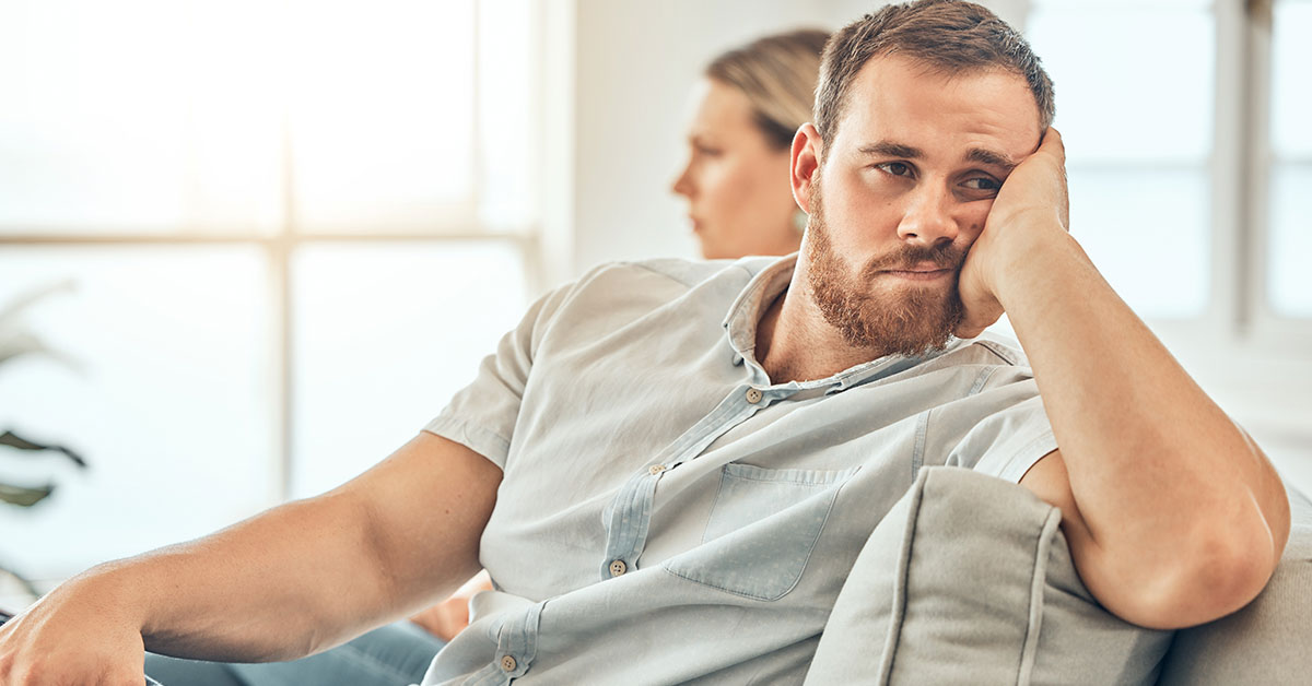 man upset with his partner, turning away from her while sitting next to her on couch