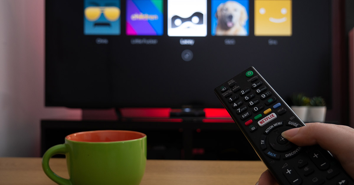 person pointing TV remote and television displaying Netflix profile screen.
