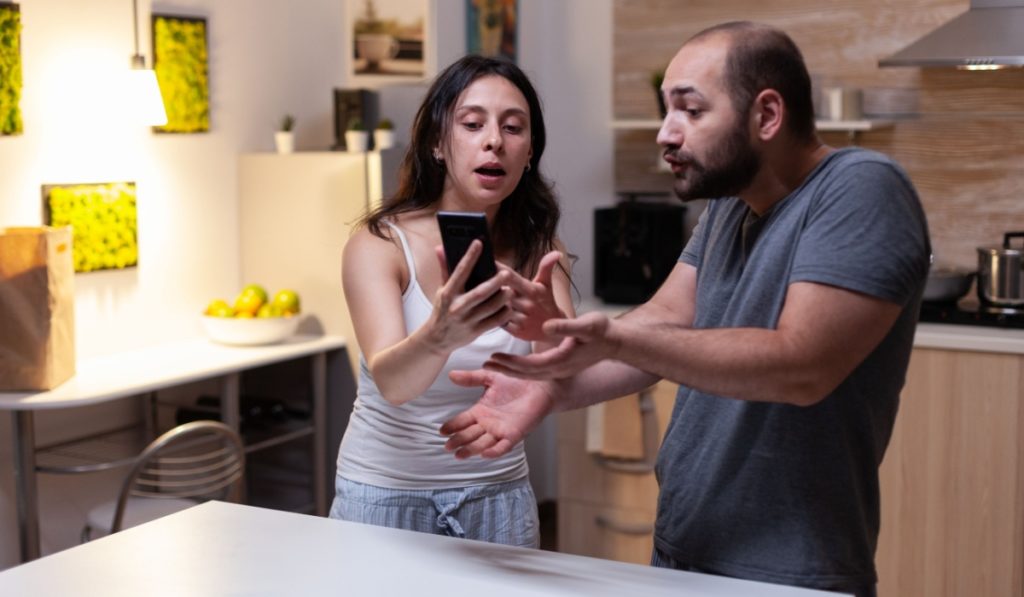 Caucasian man caught cheating by jealous wife looking at secret messages on smartphone. Couple fighting and yelling because of infidelity and trust issues. Marriage crisis, conflict