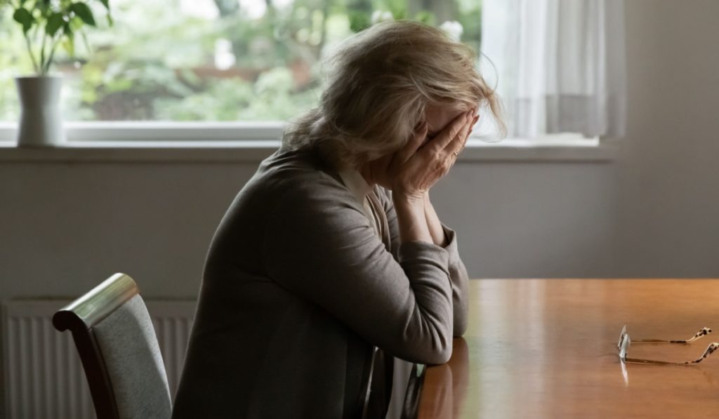 Unhappy old Caucasian woman sit at table at home cry feeling depressed sad suffer from life or health problems. Upset lonely mature female distressed with loneliness solitude, mourn yearn at home.