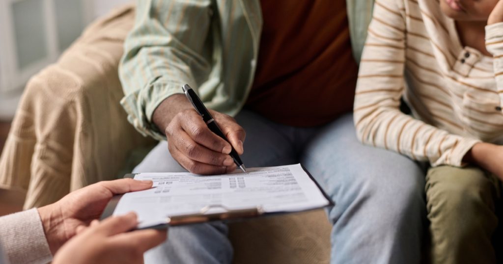 Side view closeup of unrecognizable Black man signing document on clipboard in clinic copy space