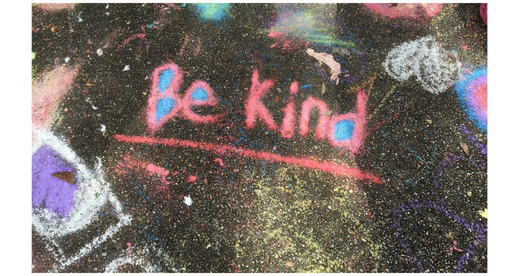 An image of a chalk drawing that says "Be Kind" with colorful shapes and spots in the background. 