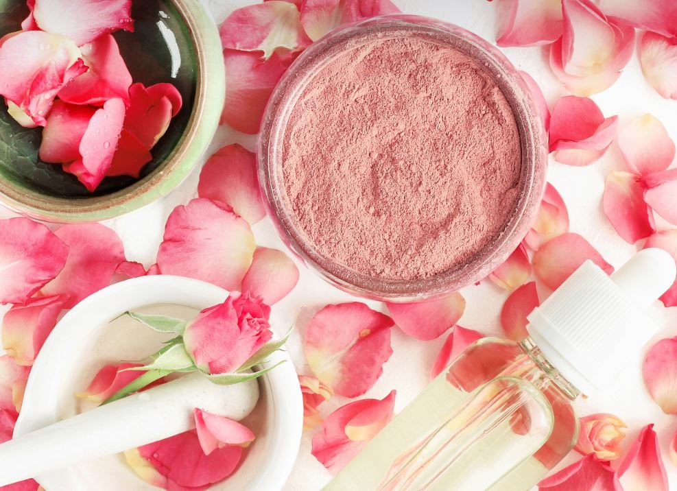 Rose powder and oil. Rose petals in the background.