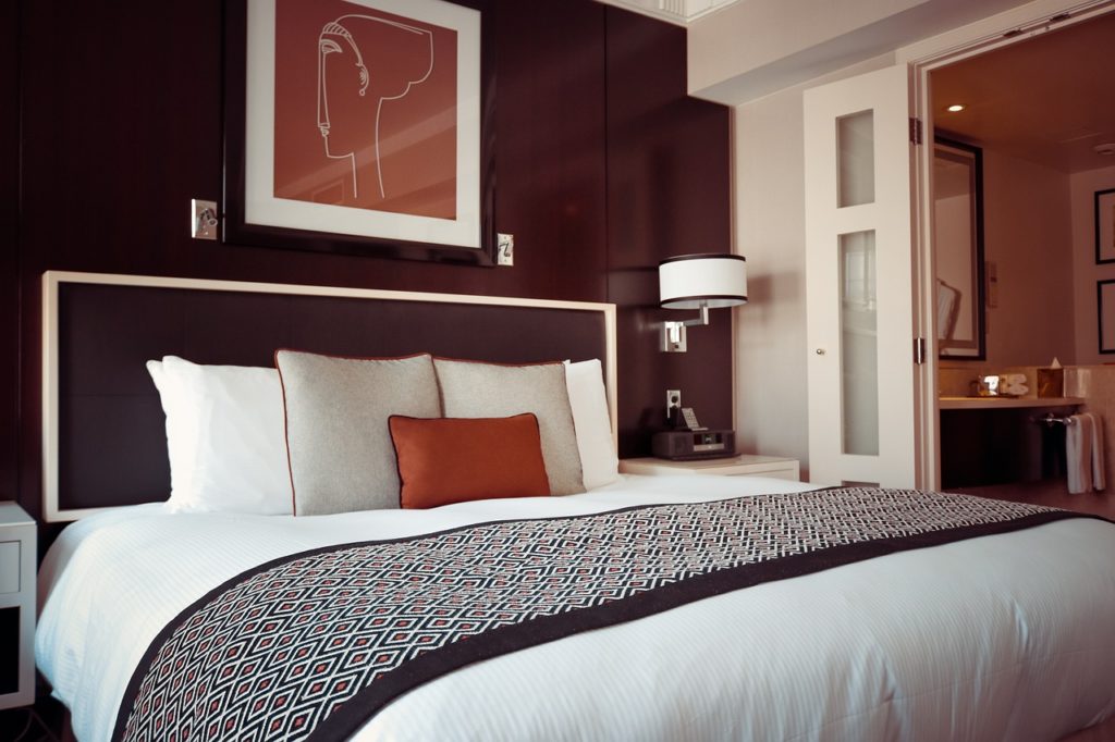 A hotel room bed with a red wall and white doorway in the background.