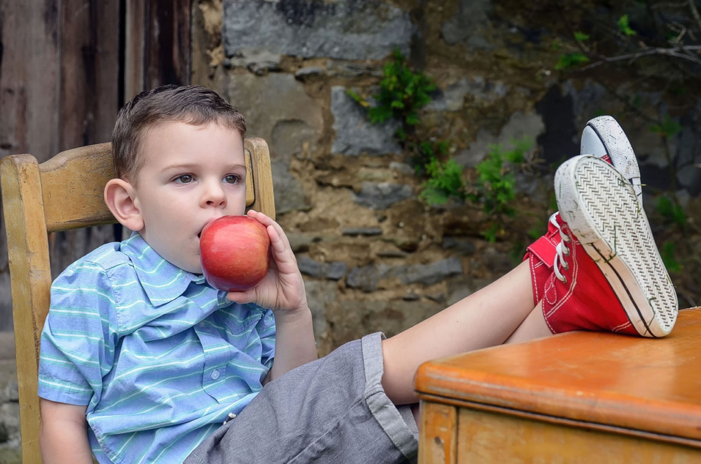 child leaning back with his feet on the table eating an apple