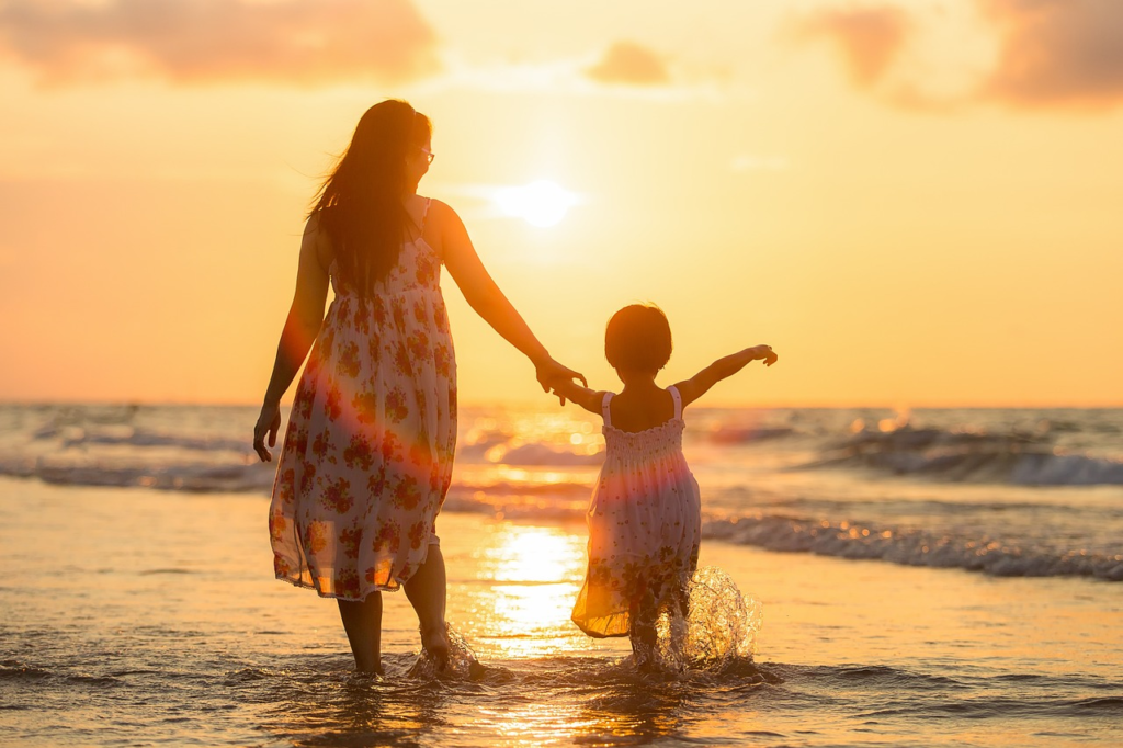 mother and daughter walking on the beach at sunset