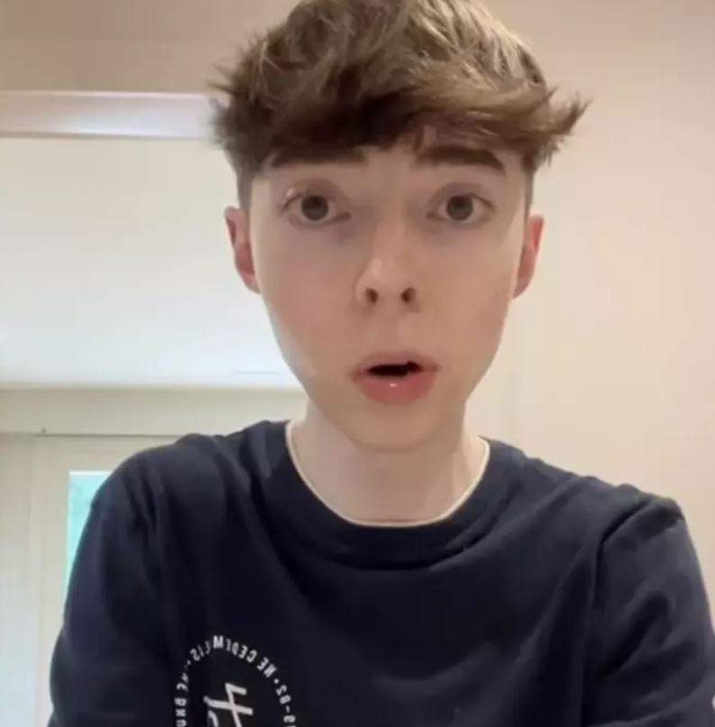 Close up of a young man wearing a black t-shirt. White walls and ceiling in the background.
