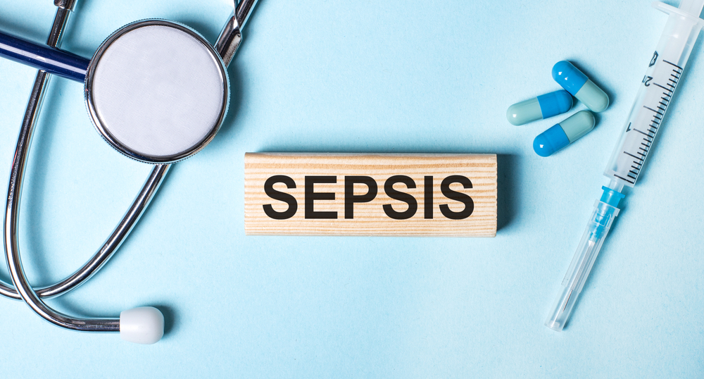 On a blue background, a stethoscope, a syringe and pills and a wooden block with the word SEPSIS. Medical concept