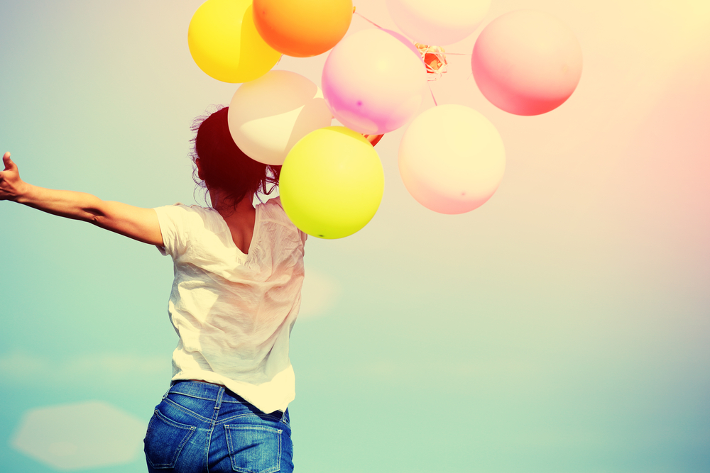 young asian woman running and jumping on green grassland with colored balloons