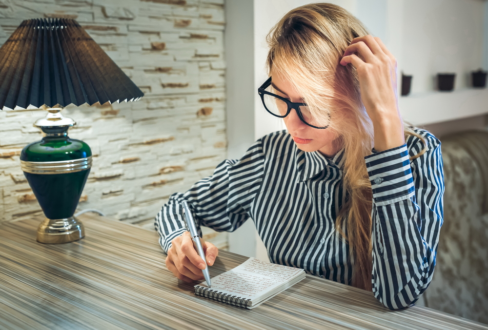 girl sitting at the table and writes in a paper notebook amounts to a list, write poetry, write down their thoughts and thinking
