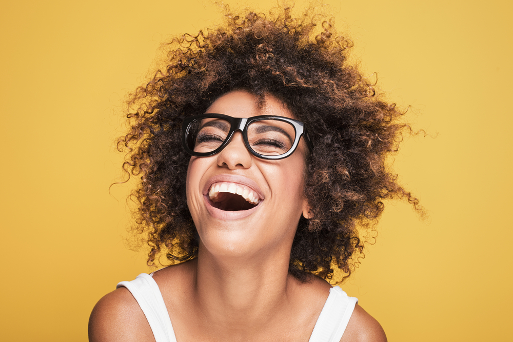 Young beautiful african american girl with an afro hairstyle. Attractive girl wearing eyeglasses. Portrait. Yellow background.