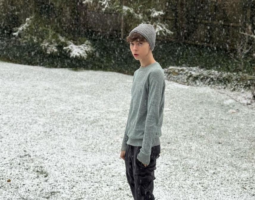 A young man standing in the snow. Trees in the background.