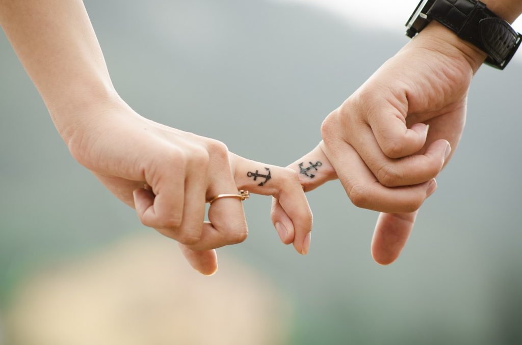 Couple's index fingers with anchor tattoos intertwined. Blurred background.