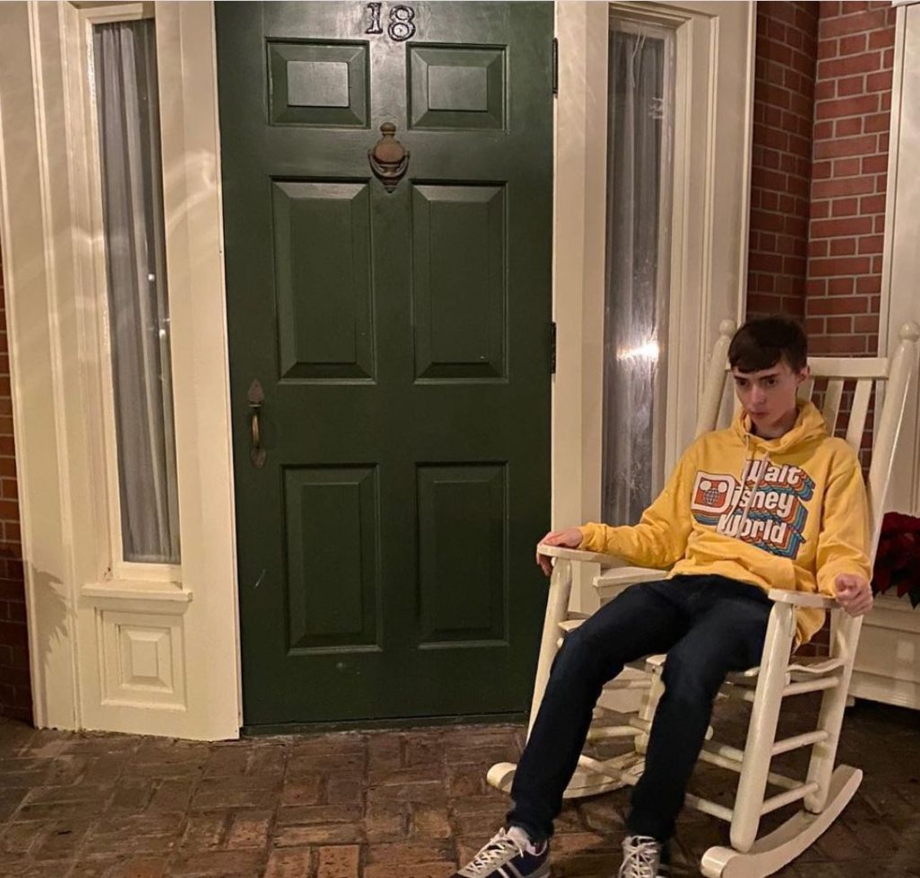 Young man sits in a rocking chair. House in the background.