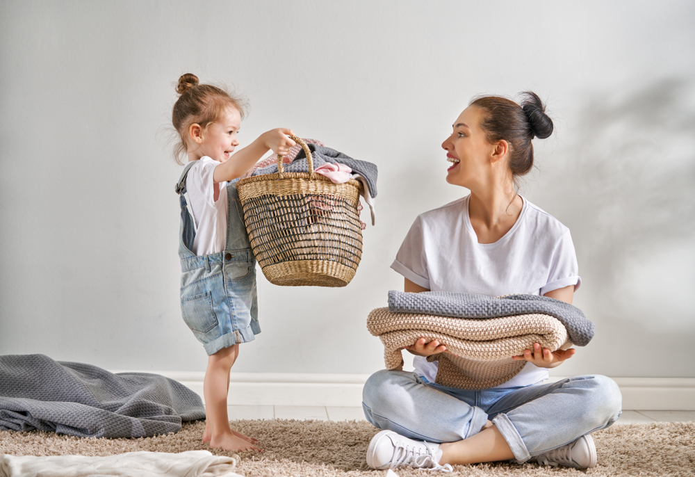 Beautiful young woman and child girl little helper are having fun and smiling while doing laundry at home.
