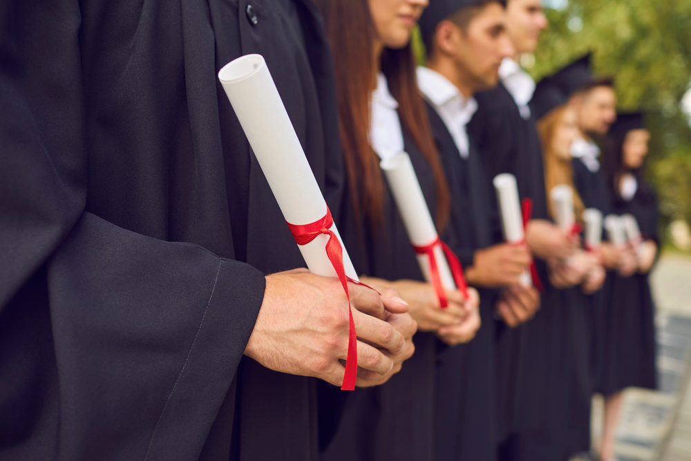 Close-up of young university graduates hands holding diplomas after university graduating outdoors, selective focus. Graduating from university or college concept
