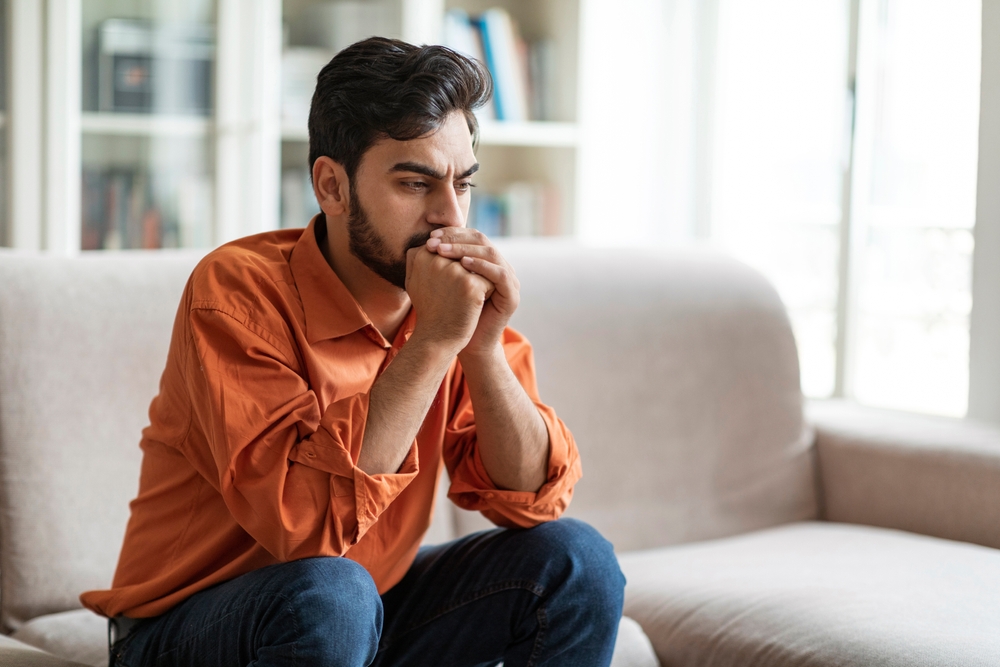Permacrisis, life problems, financial hangout concept. Pensive young middle eastern man sitting on sofa at home, leaning on his hands, experiencing difficulties in life, looking at copy space