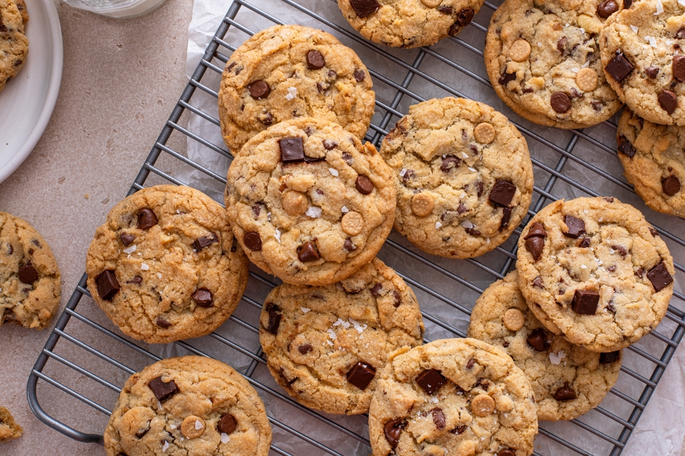 Chocolate chip cookies on a cooling rack with flaky salt served with cold milk overhead shot