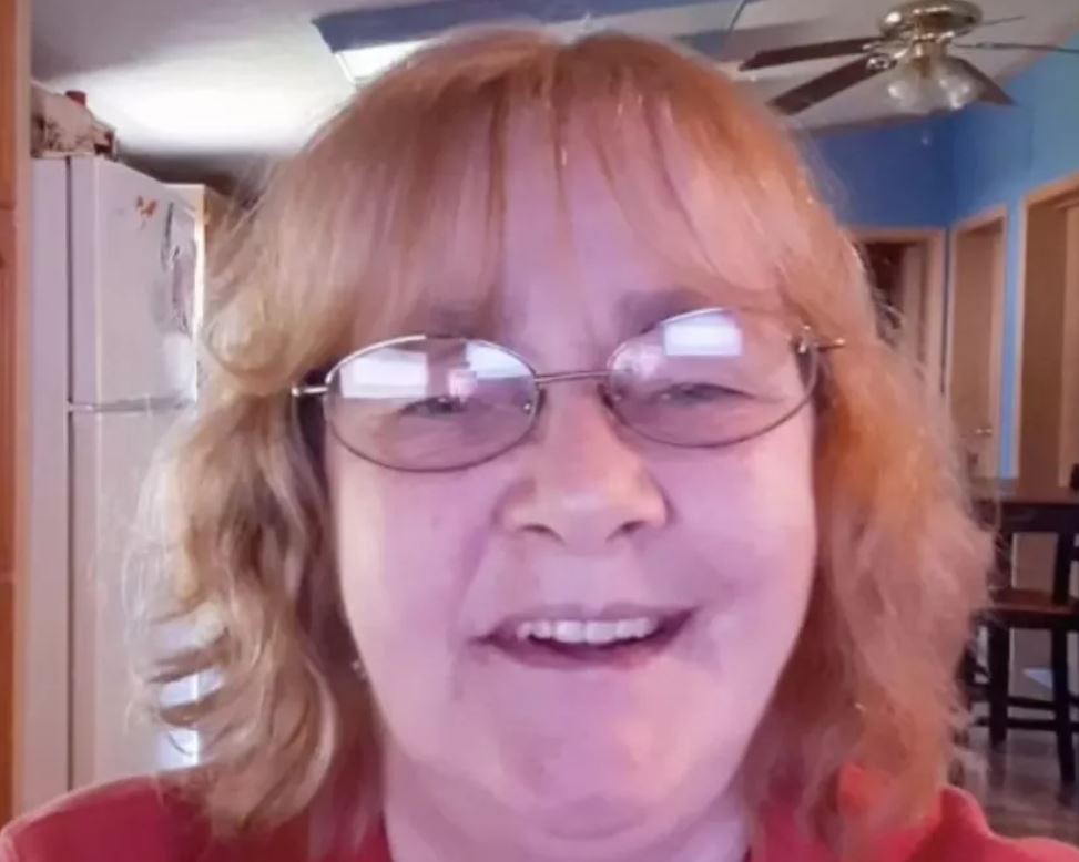 A woman taking a selfie. White fridge, blue walls, a fan, and the ceiling in the background.