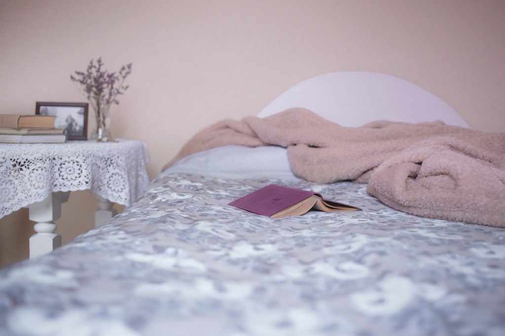A bed with a fuzzy oink blanket. A side table with flowers and books in the background.