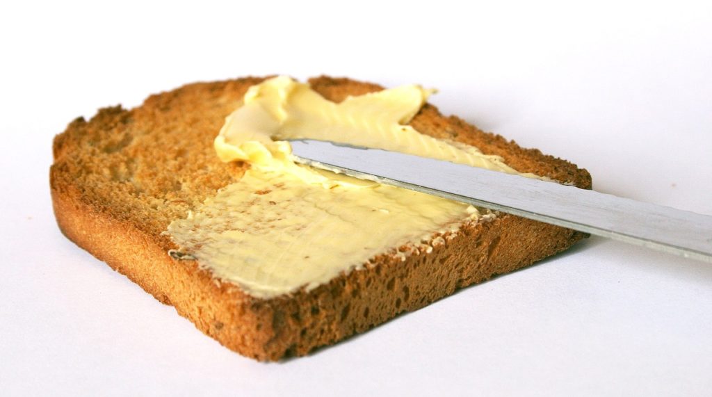 A knife spreading butter on toast. White background.