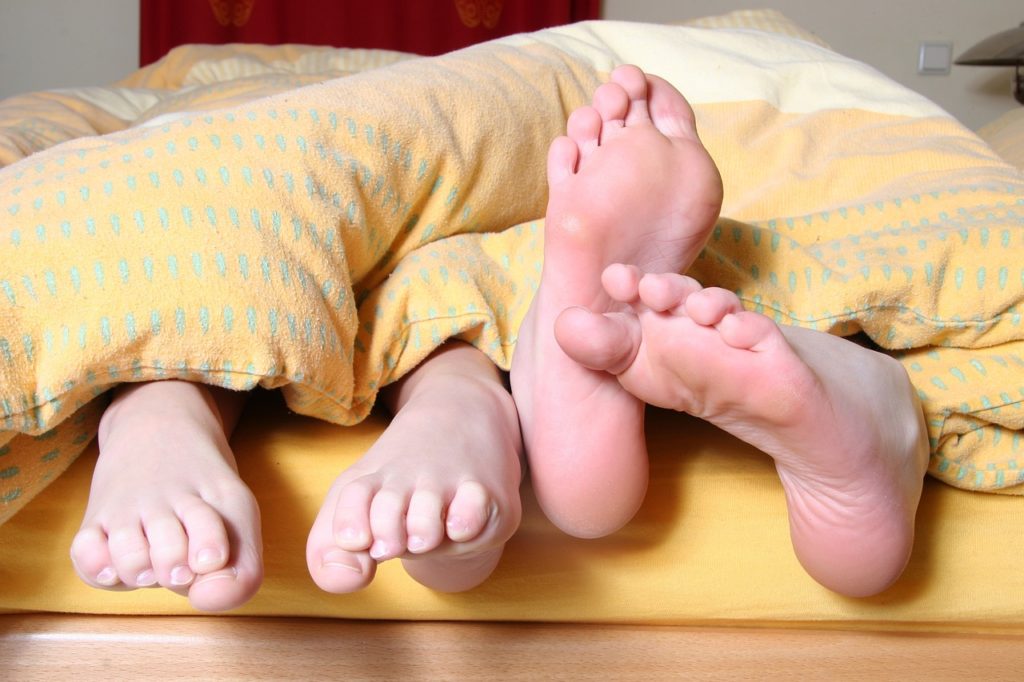 Two people with their feet hanging off the bed.