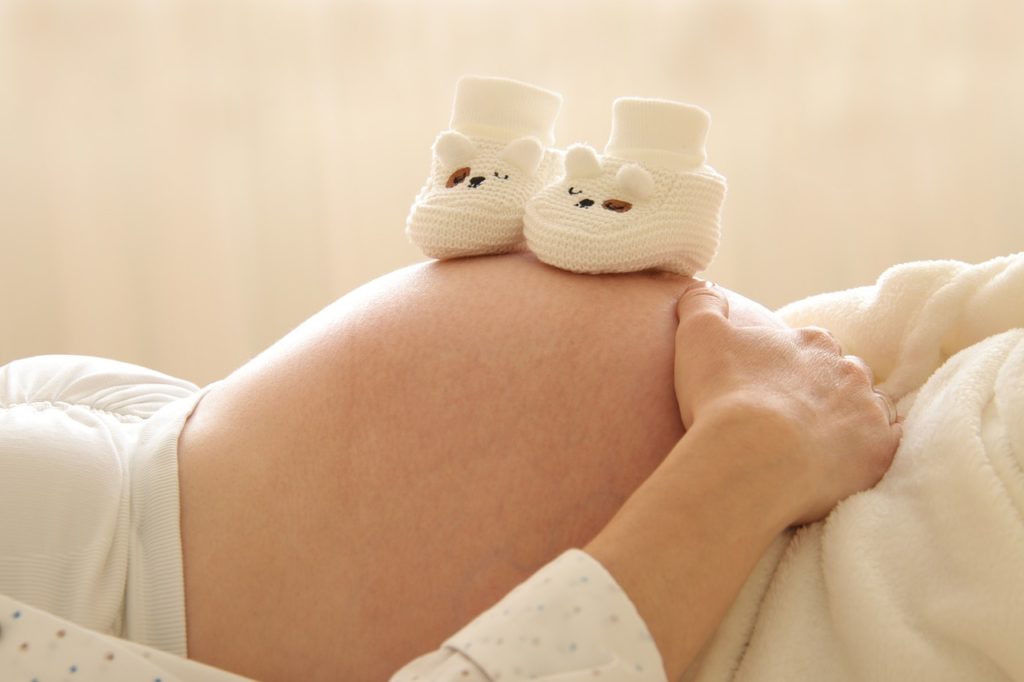 A pregnant belly with white fuzzy baby shoes.