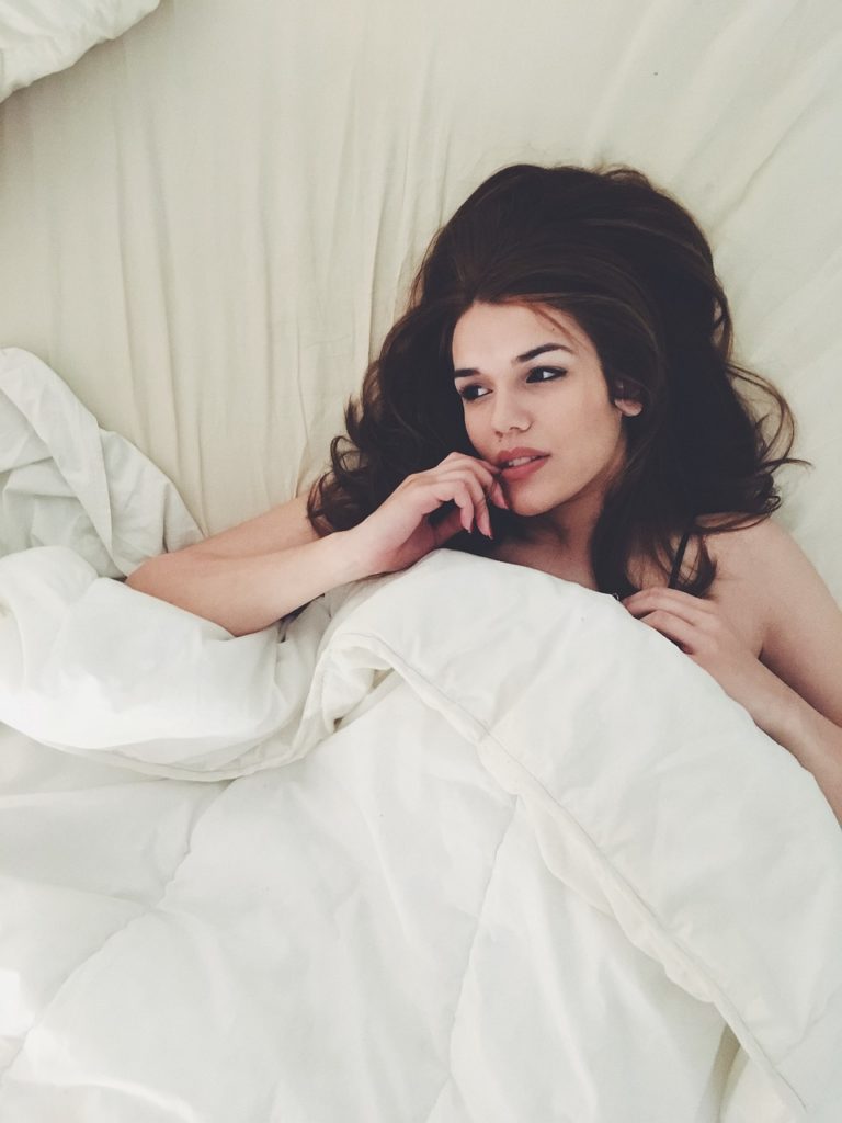 A woman lying in bed. White sheets in the background.