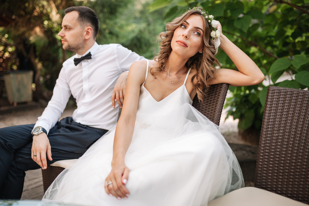 Newlywed coupe sitting on a sofa angry at each other in a middle of an argument. Young couple problem concept outdoor.
