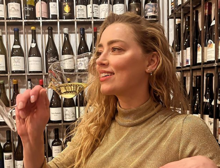 amber heard drinking wine while wearing a gold outfit