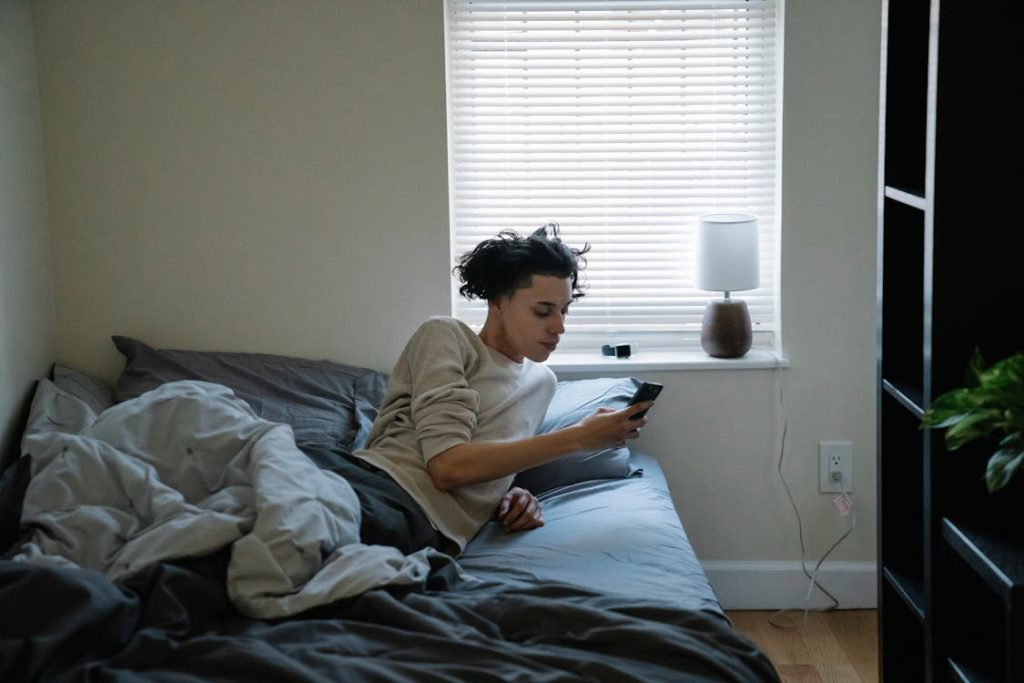 man chatting on smartphone in bed at home
