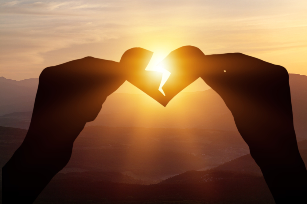Two hands hold a broken heart on the background of the sunset. Concept of love feelings