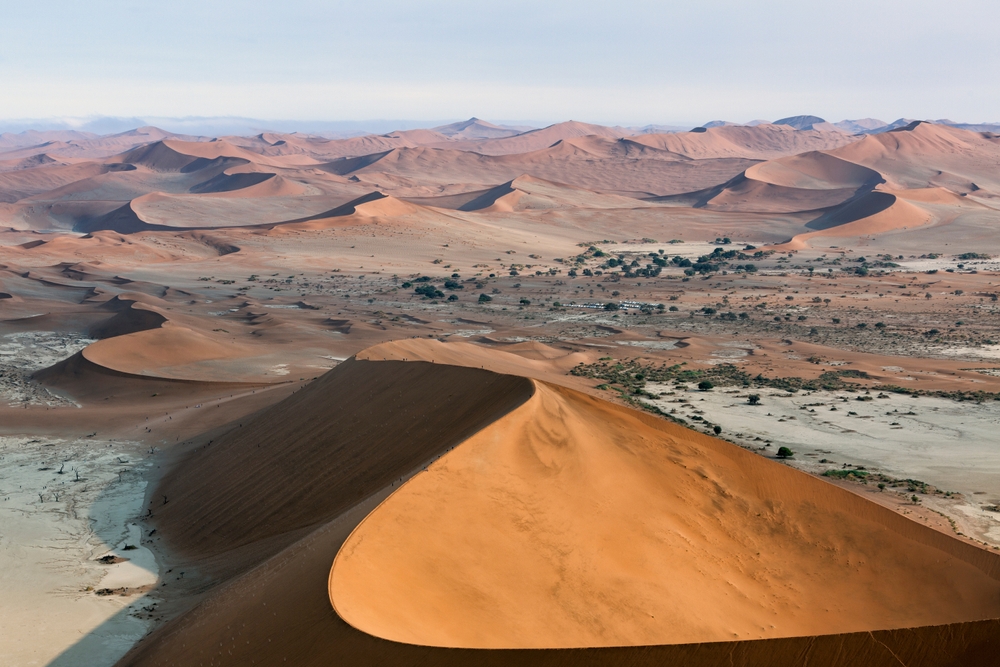 Namibia landscape with sand hills and dunes in Sossusvlei, Namib-Naukluft National Park, Namibia. Panorama of Namib desert with tourists walking up to red sand dunes at sunrise.