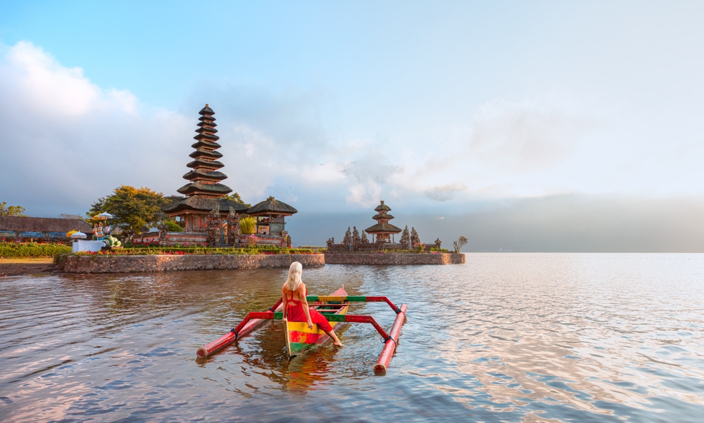 Young blonde girl in traditional red dress in the boat near Pura Ulun Danu Bratan temple - Hindu temple on Bratan lake - Bali island, Indonesia