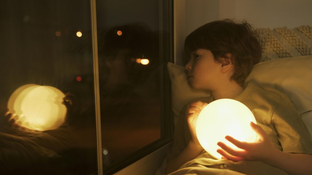 kid in his bed holding a moon light