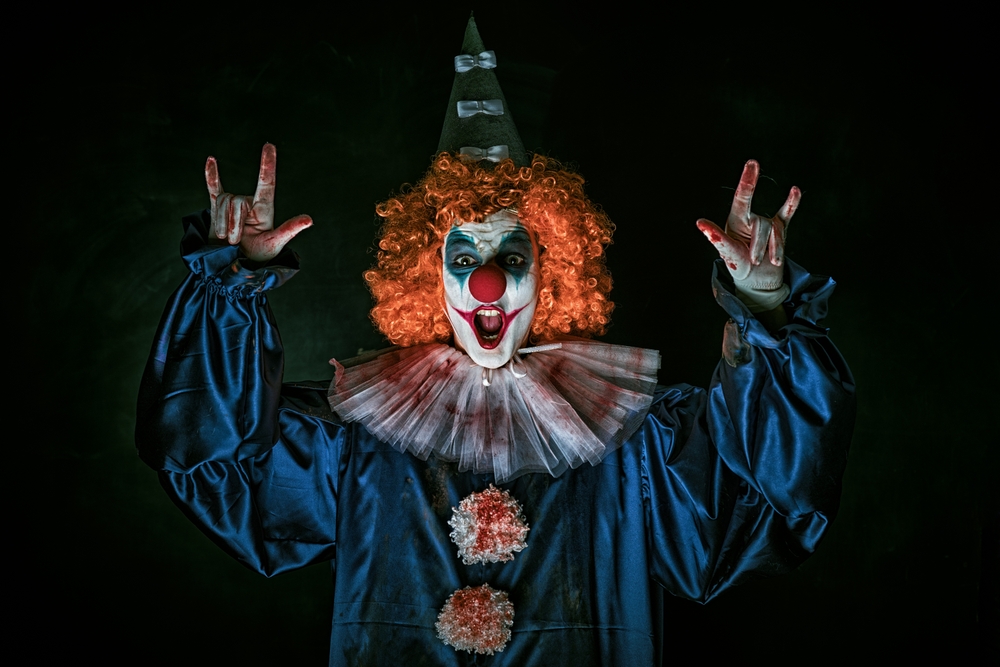 Portrait of a creepy scary clown in a bloody circus costume and a red wig. Black background. Horror. Halloween.

