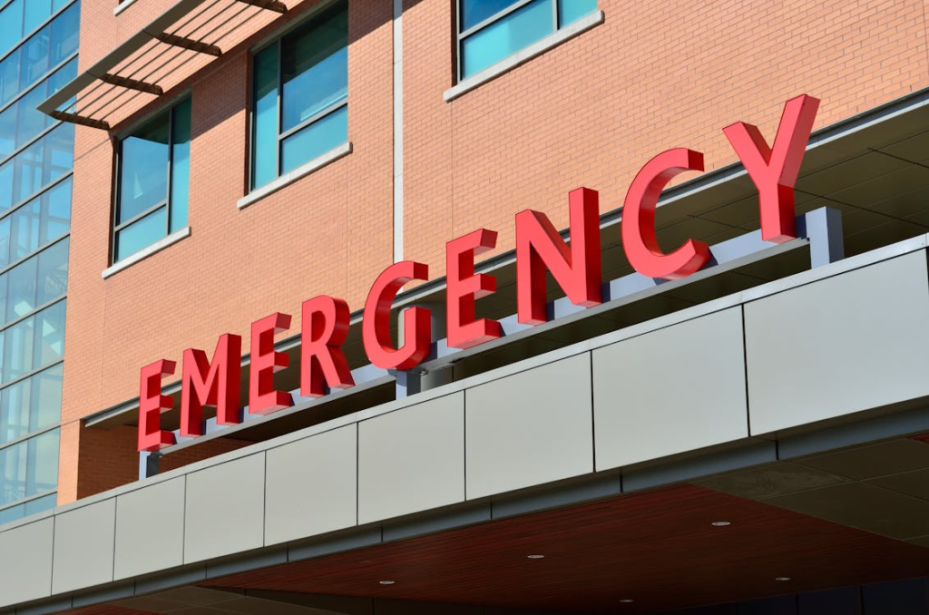 Exterior of a hospital emergency entrance with large red 'EMERGENCY' lettering on a brick building.