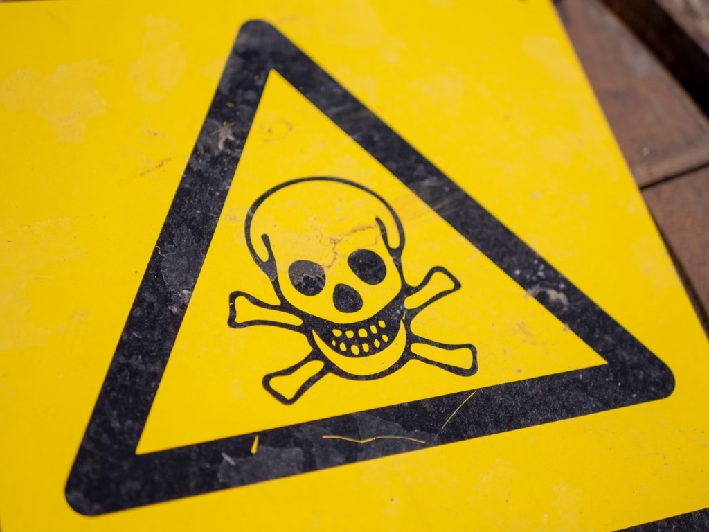 Close-up of a yellow hazard warning sign featuring a skull and crossbones symbol, indicating danger. This warning symbol represents the hidden dangers of seemingly harmless household items when misused.