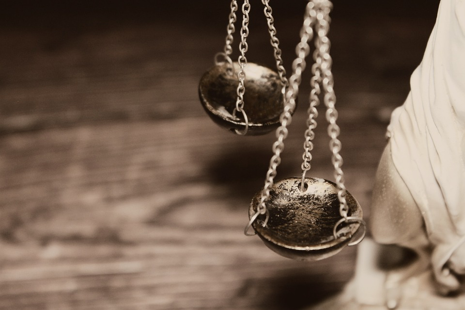 An antique brass balance scale with two weighing pans suspended by chains against a blurred wooden background, representing the justice system in the case where a father kills sex offender in Minnesota.
