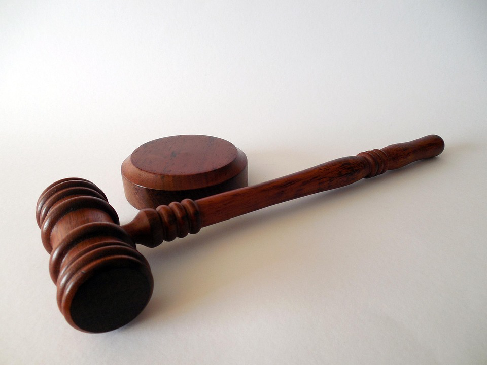 A polished wooden judge's gavel with its round sound block on a plain white background, symbolizing the legal proceedings in the court case.