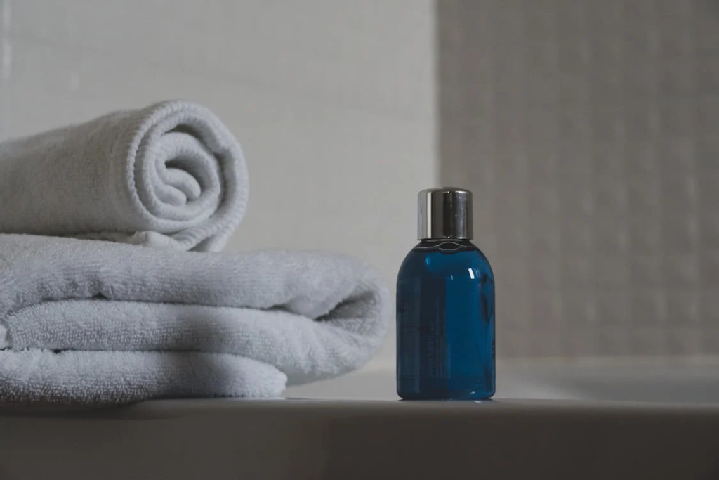 Blue shampoo bottle next to folded white towels in bathroom setting.