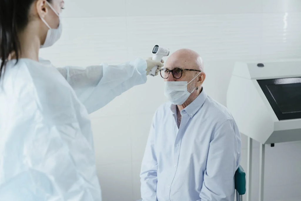 A healthcare worker taking the temperature of an elderly man during a health screening, demonstrating the preventive Medicare benefits that include annual wellness visits and health assessments.